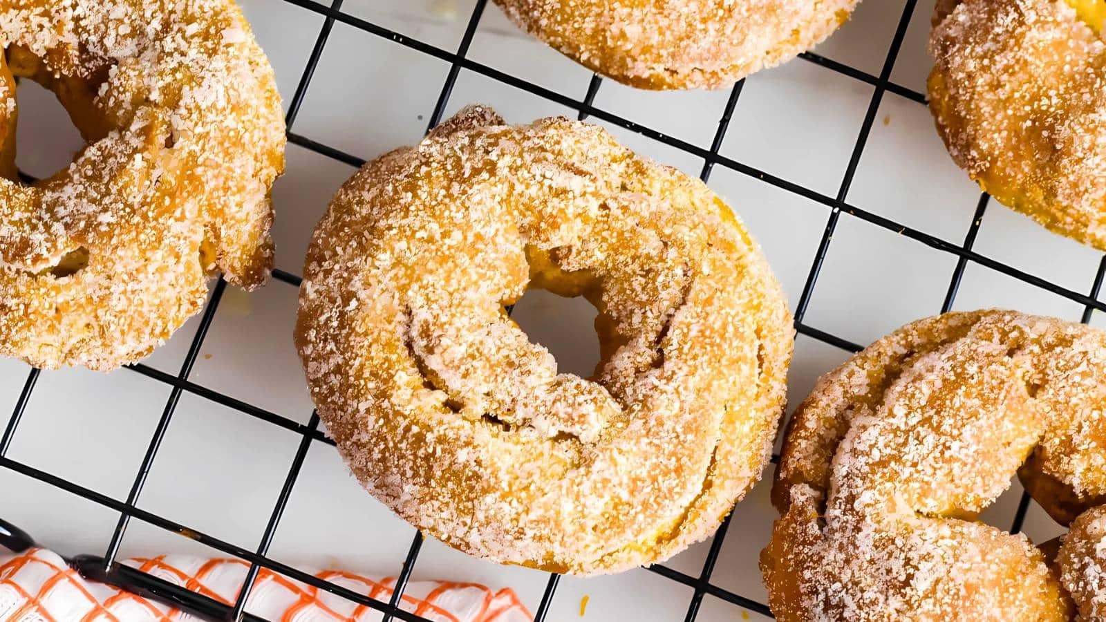 Close-up of ring-shaped pastries dusted with powdered sugar, cooling on a black wire rack.