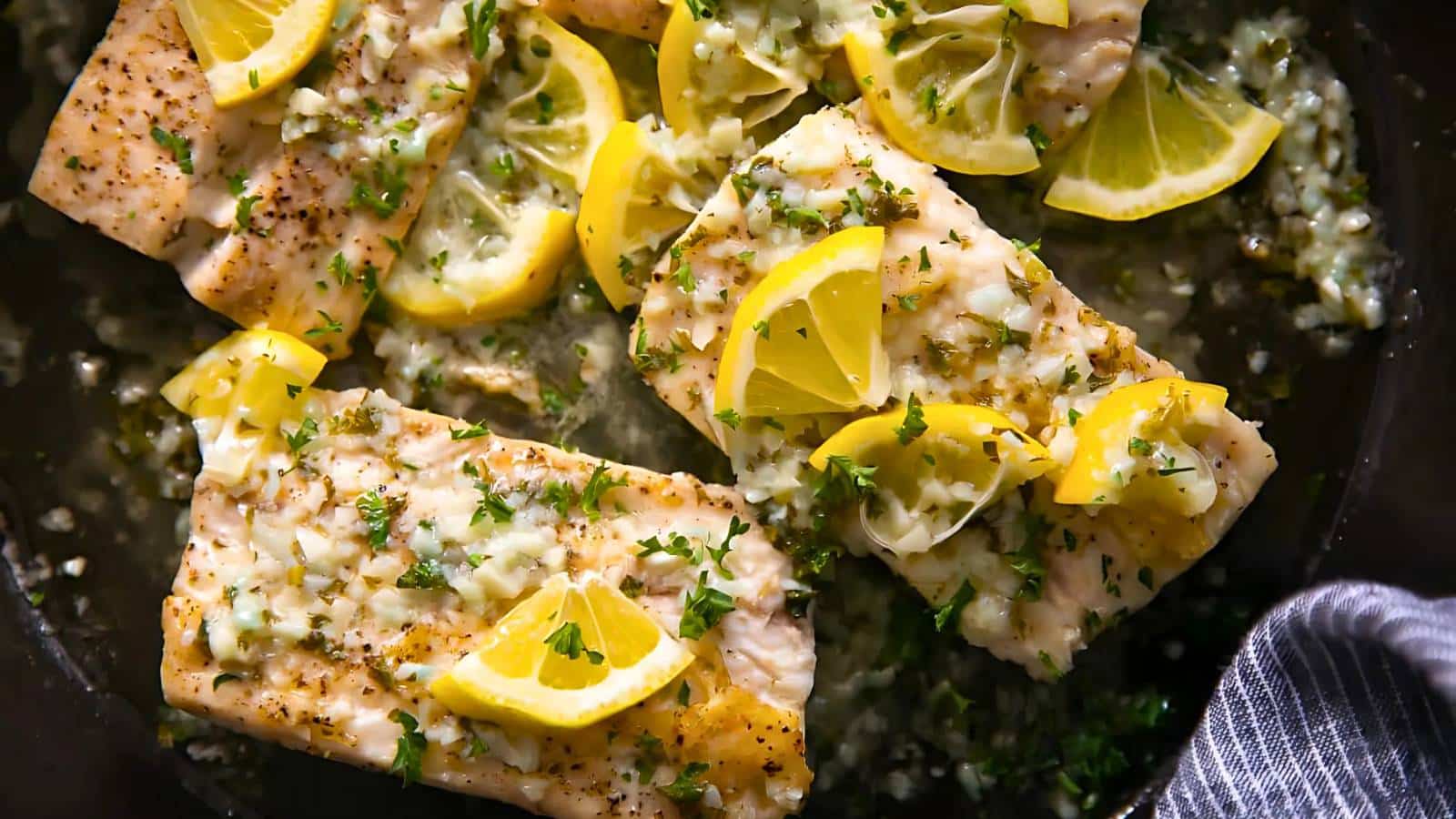 Cooked fish fillets garnished with lemon slices and herbs in a pan.