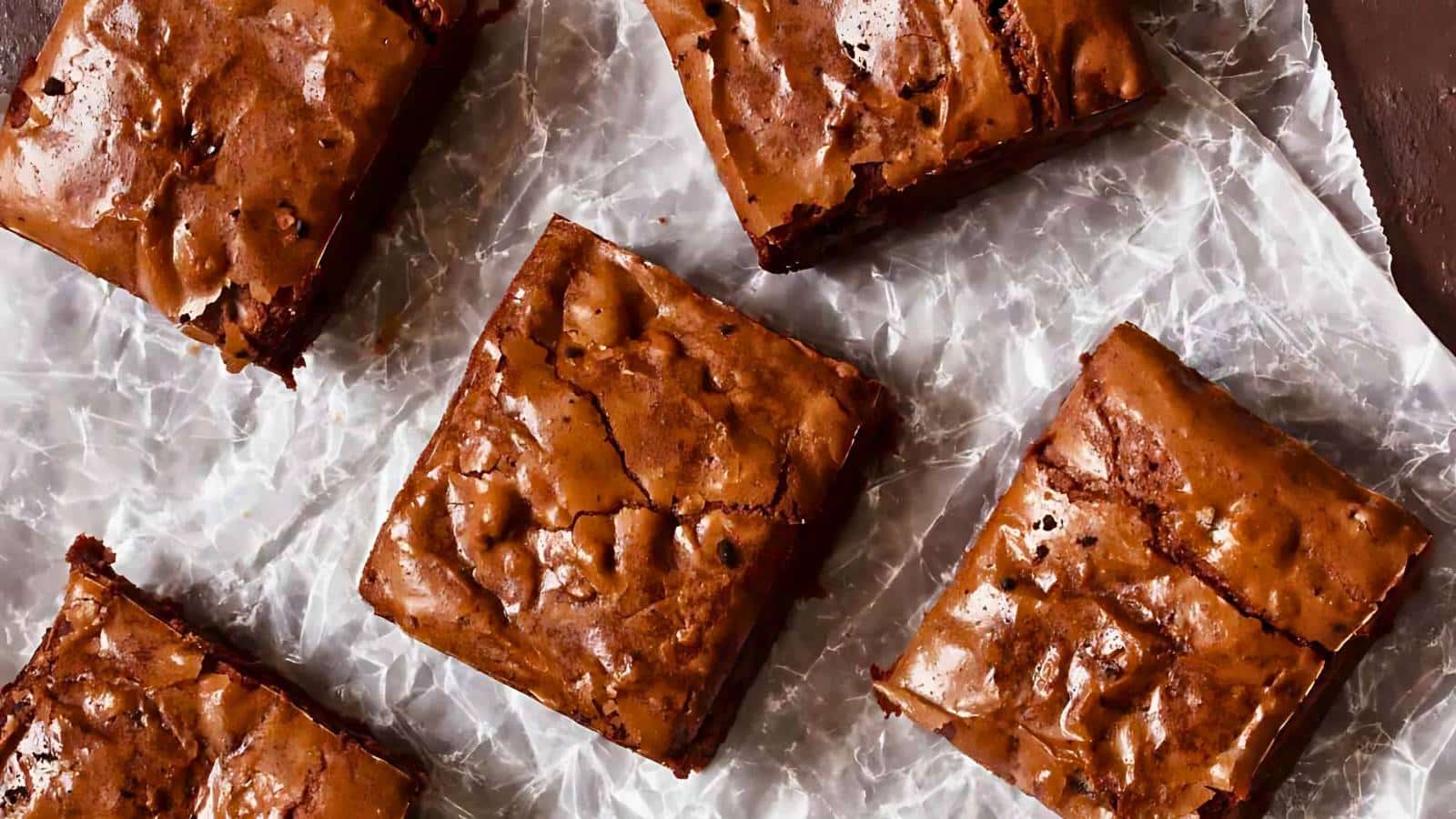Five fudgy chocolate brownies on crinkled parchment paper.