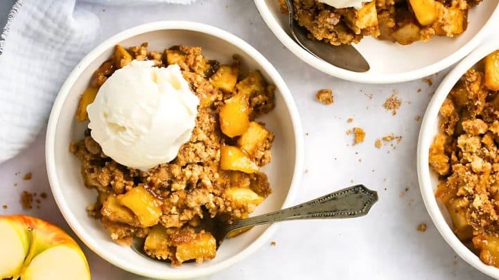 A bowl of apple crumble topped with a scoop of vanilla ice cream, with a spoon beside it.