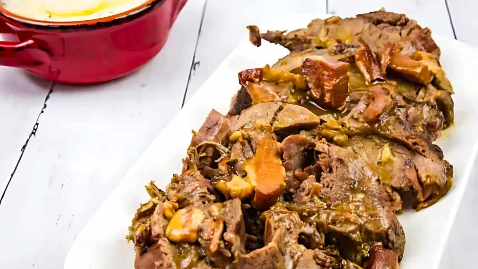 A plate of cooked beef with mushrooms, next to a red dish on a white wooden table.