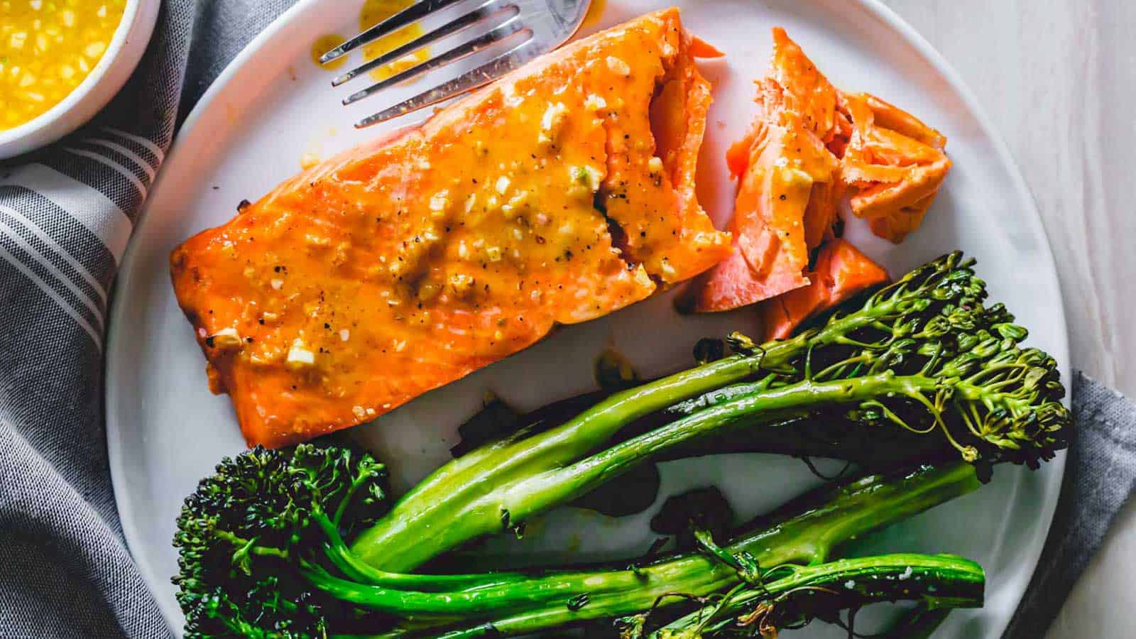 A plate with cooked salmon and roasted broccolini, accompanied by a fork and knife on the side.