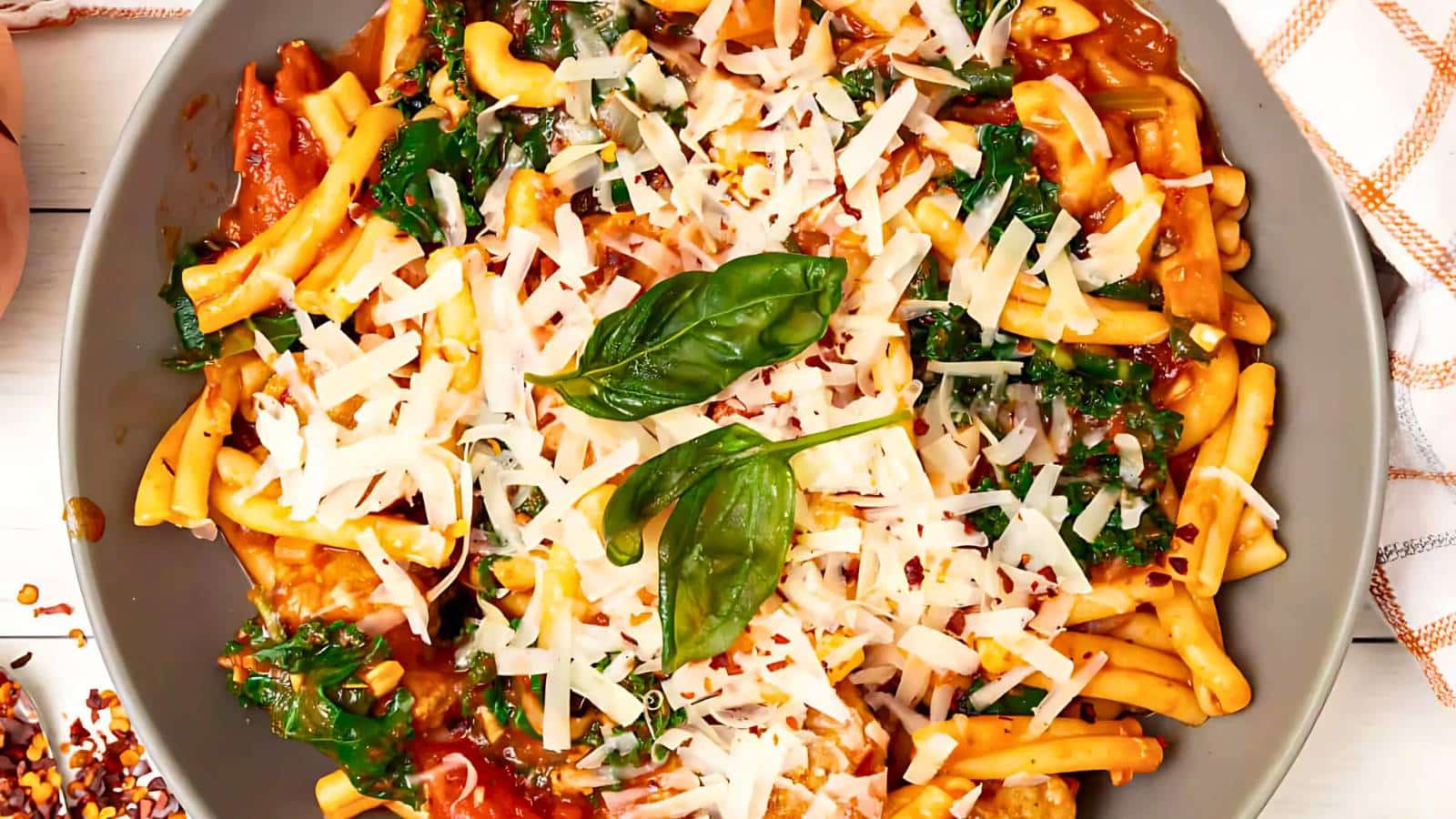 A plate of pasta topped with tomato sauce, grated cheese, spinach, and basil leaves.