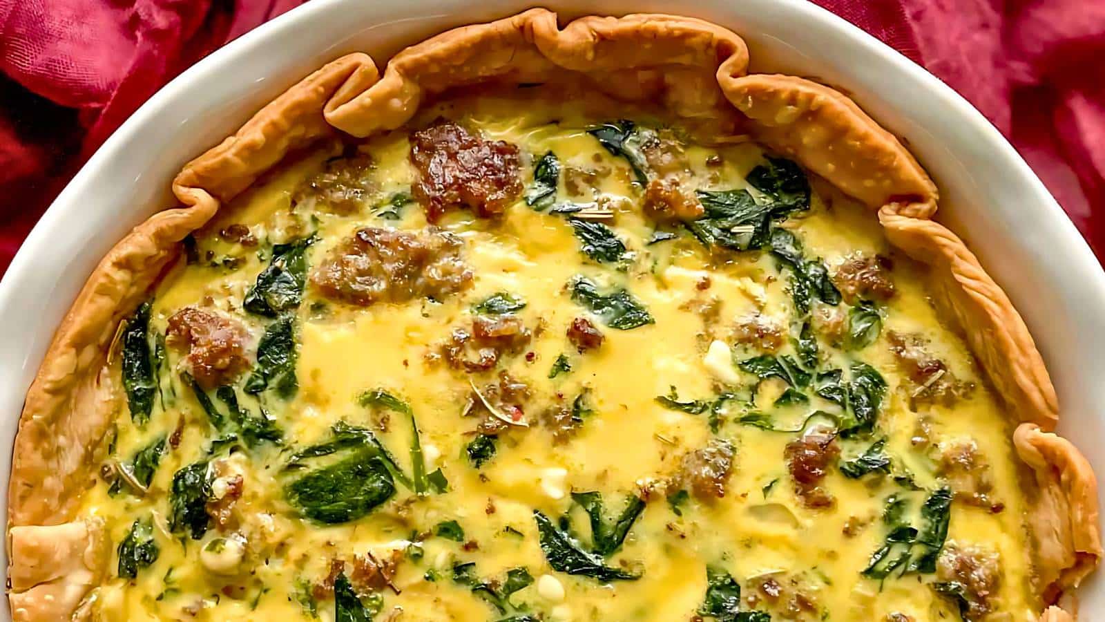 A quiche with sausage, spinach, and a golden crust, served in a white dish.