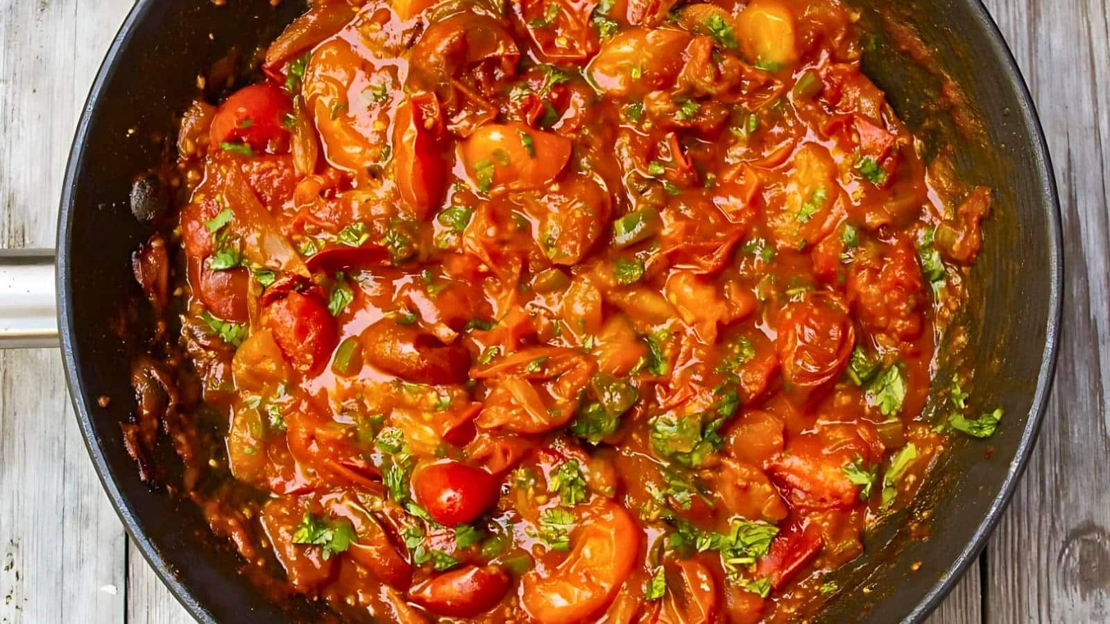 A pan filled with a vibrant and chunky tomato sauce, garnished with fresh herbs and cooked to a rich, red consistency.