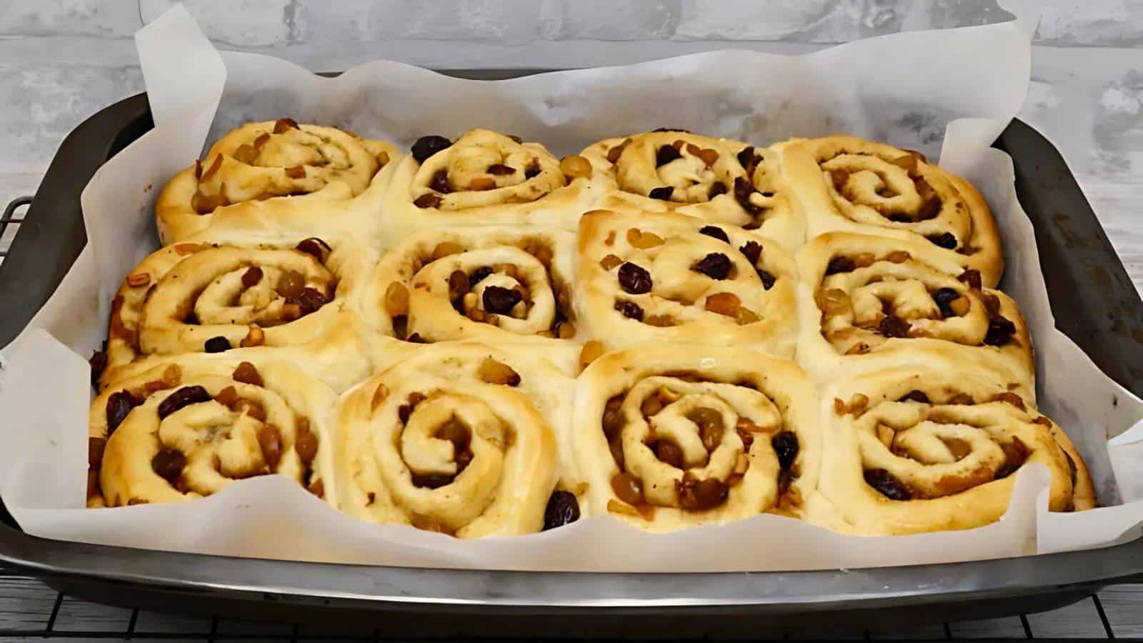 Four green cookies with white chocolate chips and dried cranberries on a dark plate, surrounded by scattered ingredients on a textured surface.
