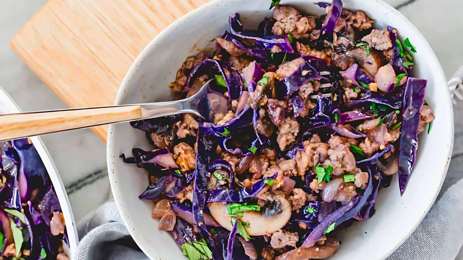 A bowl of orange lentil soup garnished with a bay leaf is placed on a white table with a silver spoon nearby.