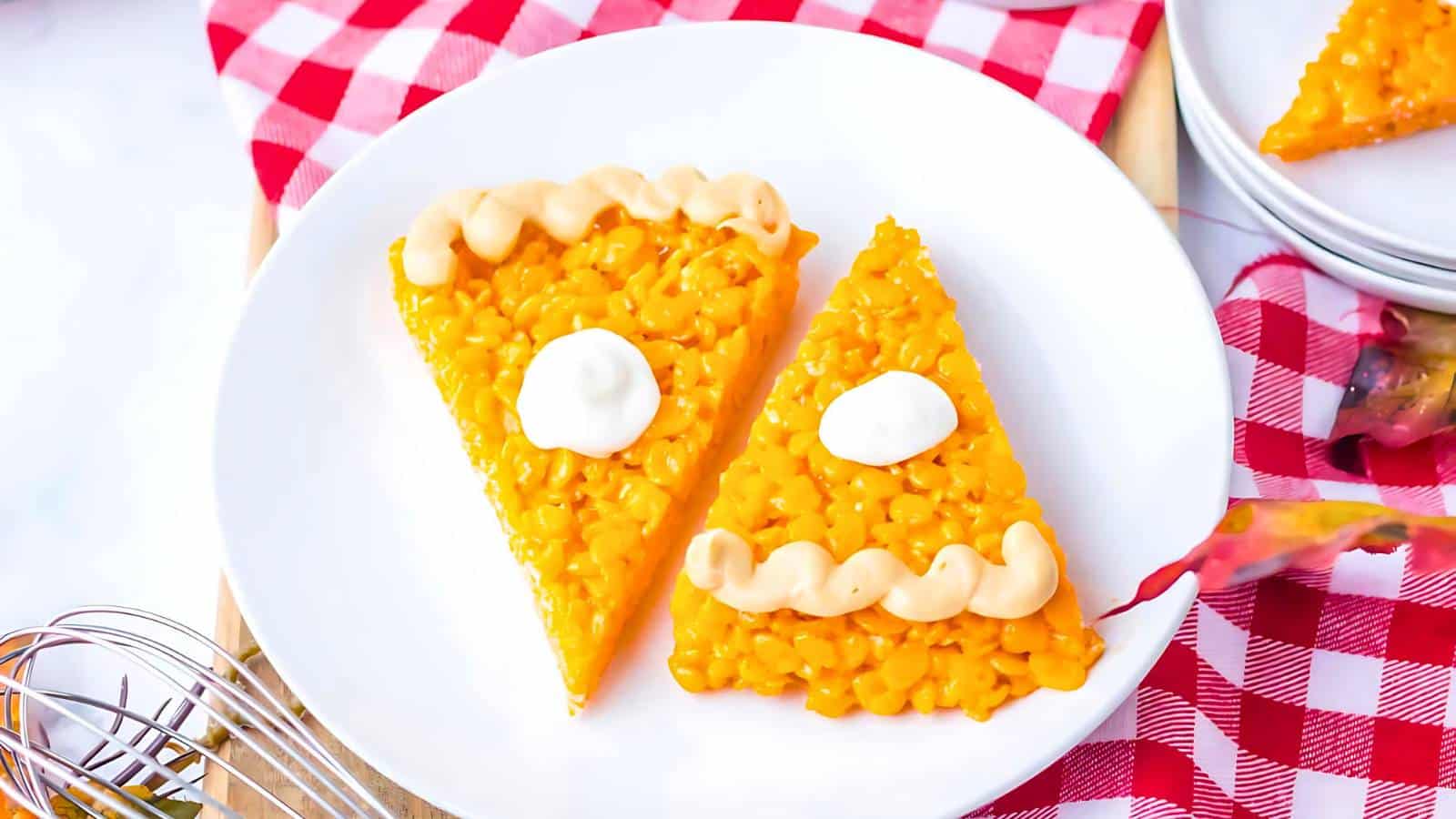 Two triangular slices of corn cake with frosting and cream dollops on top sit on a white plate, placed on a red and white checkered cloth.