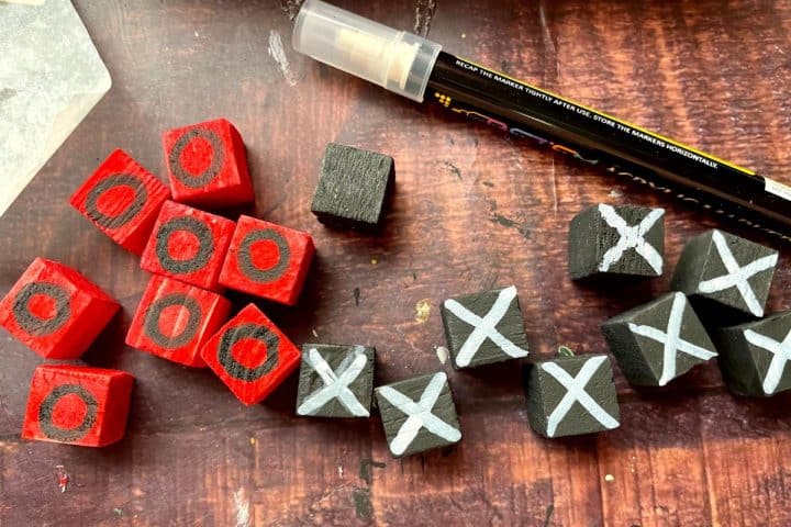 Several small wooden blocks, some painted red with black circles and others painted black with white Xs, are scattered on a table. A paint marker is also visible on the table.