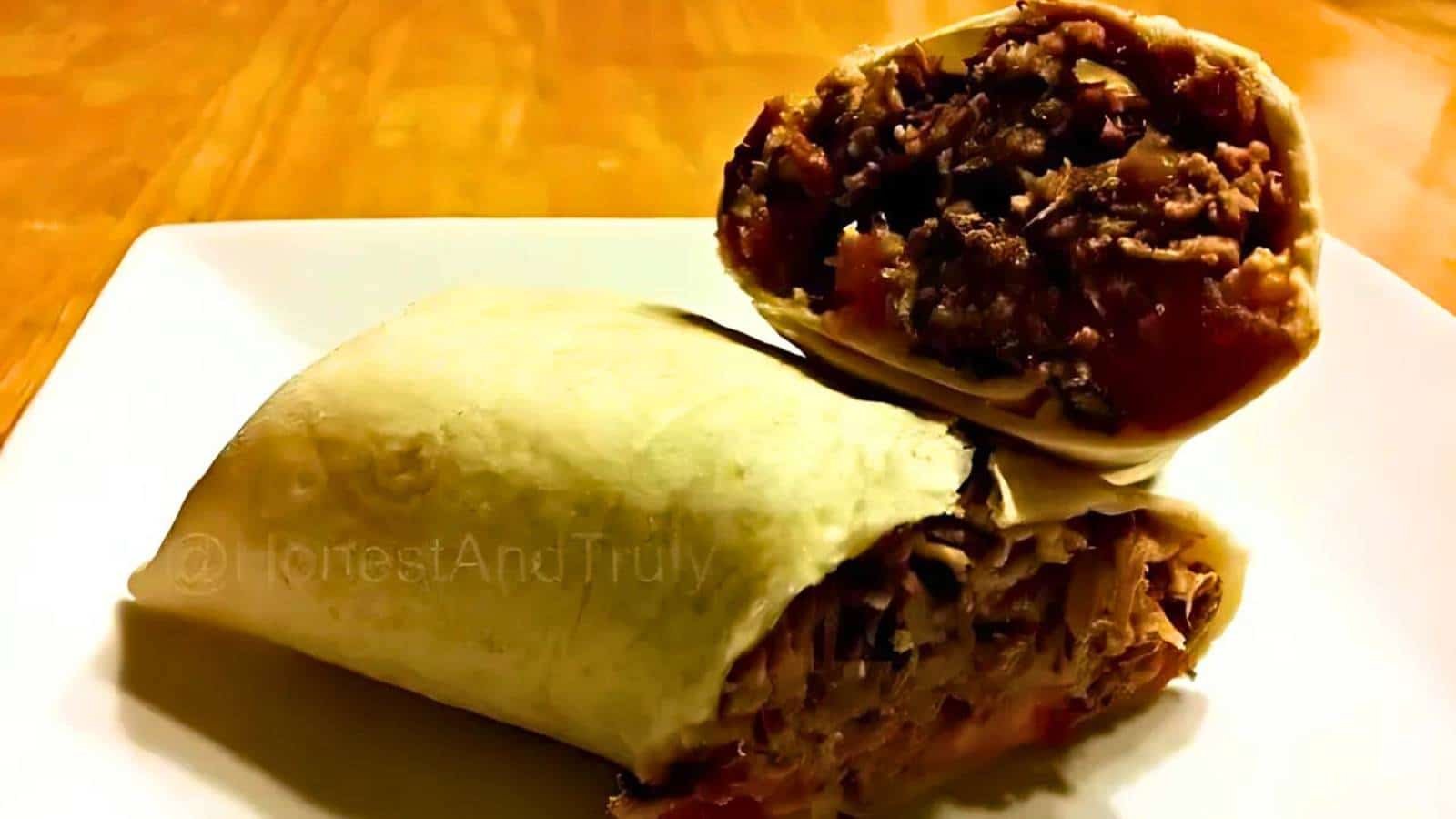 A burrito cut in half, revealing a filling of shredded meat and vegetables, is placed on a white plate.