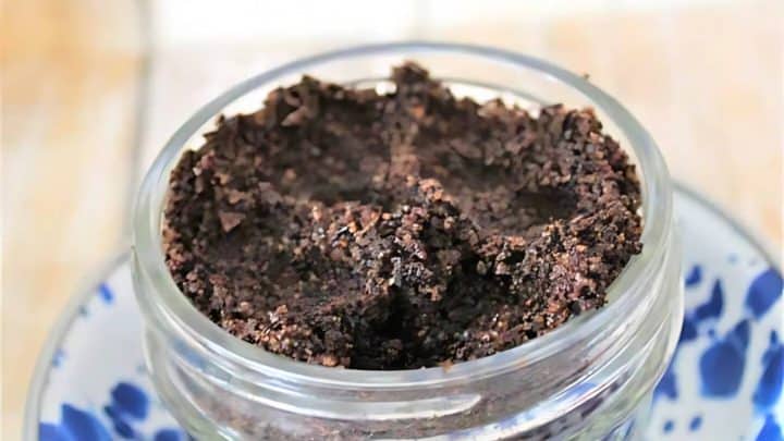 A glass jar filled with dark coffee grounds sits on a blue and white patterned plate.