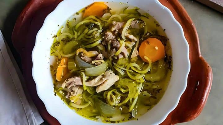 A bowl of vegetable and chicken soup with carrots, onions, and herbs in a clear broth.