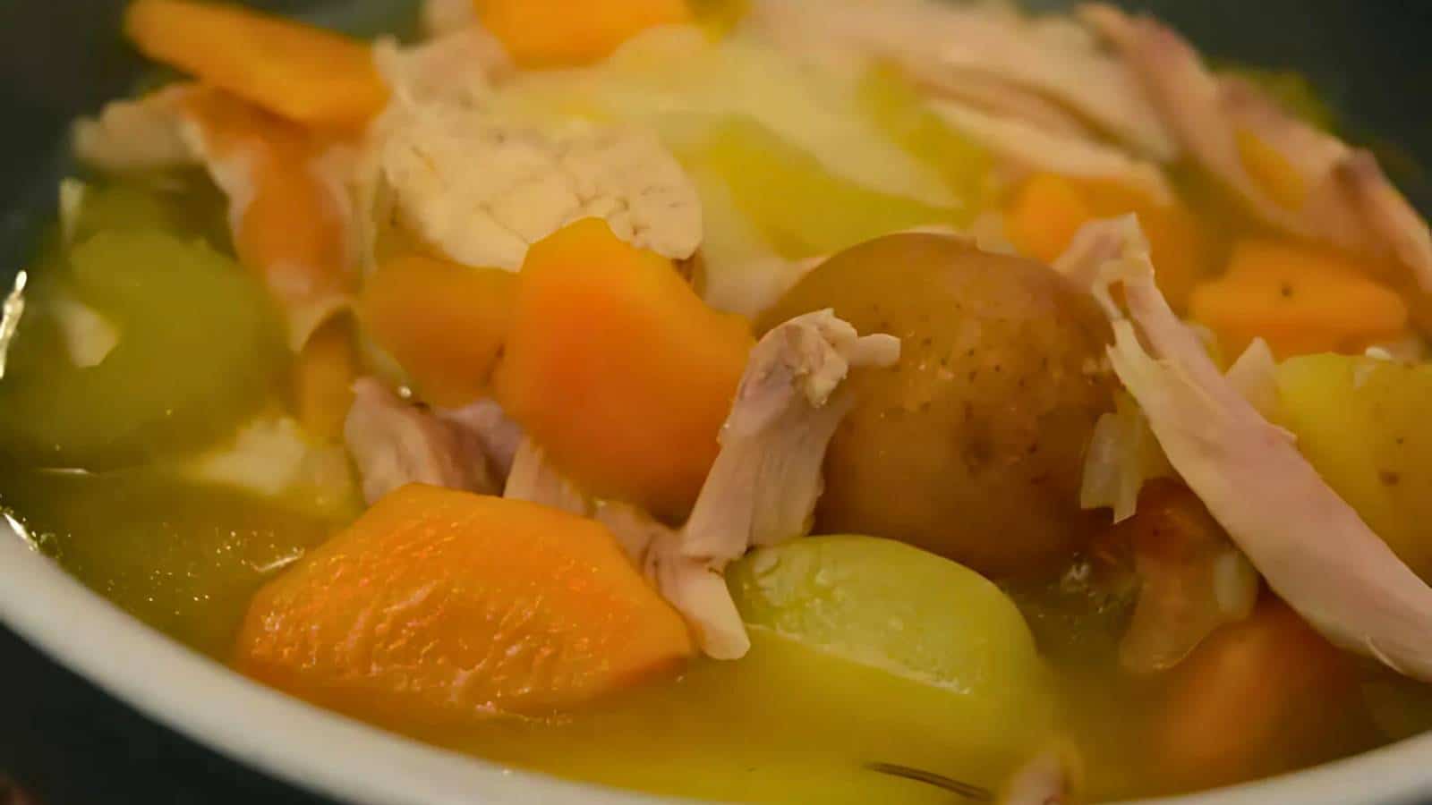 A bowl of soup containing chunks of chicken, carrots, potatoes, and other vegetables in a clear broth is the epitome of comfort foods.