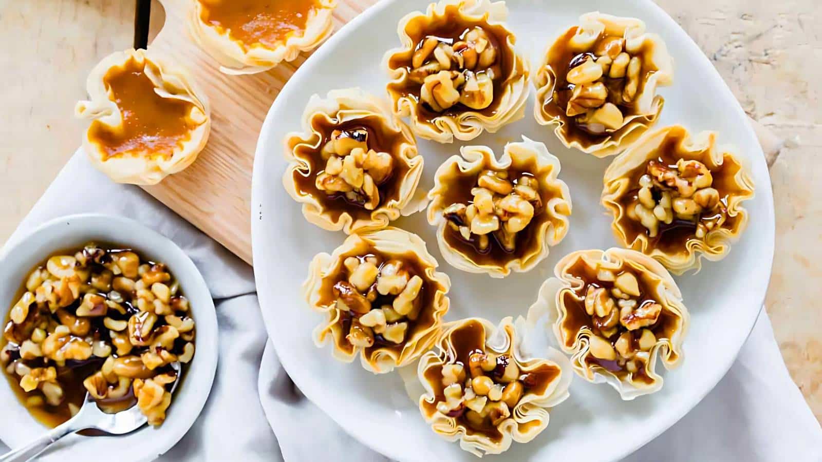 A plate of phyllo pastry cups filled with caramel and nuts, next to a small bowl with more filling and a spoon.