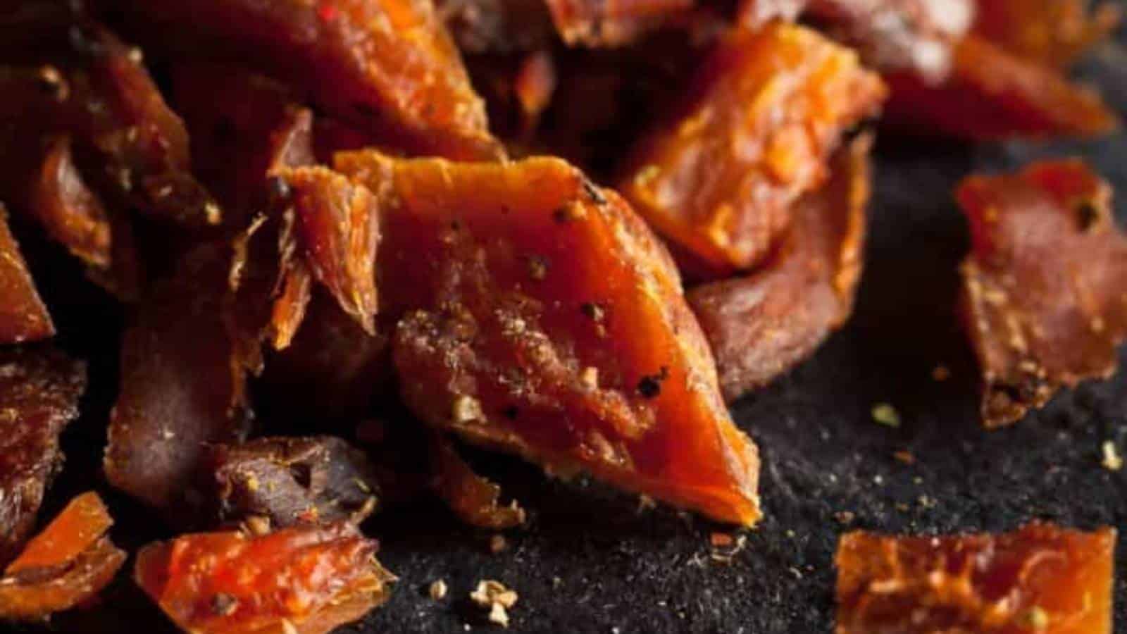 Close-up of broken, spiced beef jerky pieces on a dark surface.