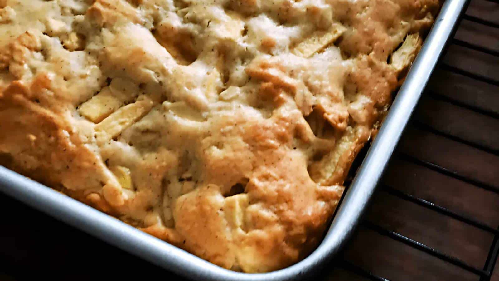 A close-up of a freshly baked apple cake in a rectangular baking dish, sitting on a cooling rack.