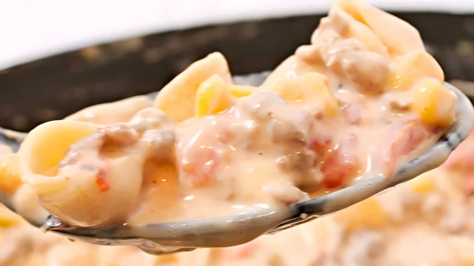 Close-up of a spoonful of creamy pasta with ground meat and diced tomatoes.