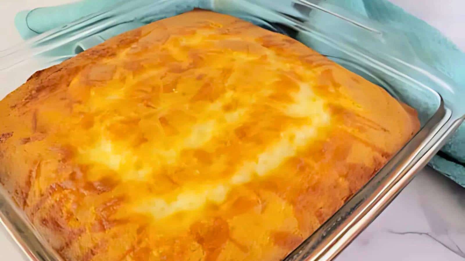 A golden-brown, baked cheesecake in a square glass dish on a marble surface, partially covered with a blue cloth.