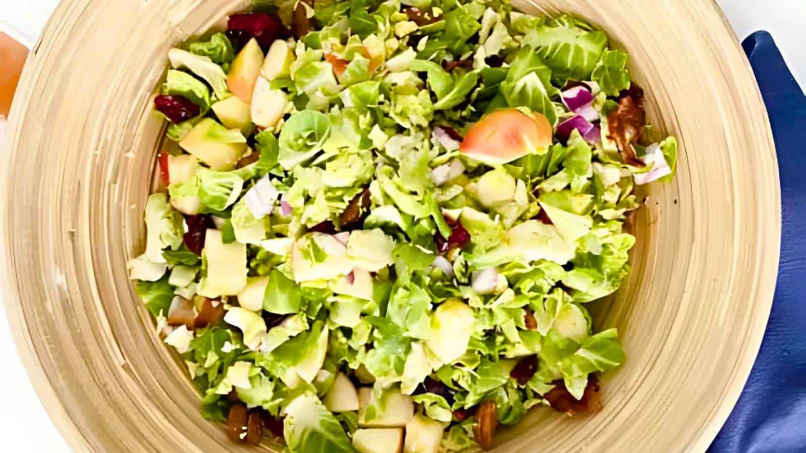 A wooden bowl filled with a mixed salad, including lettuce, apple chunks, walnuts, red onions, and cranberries.