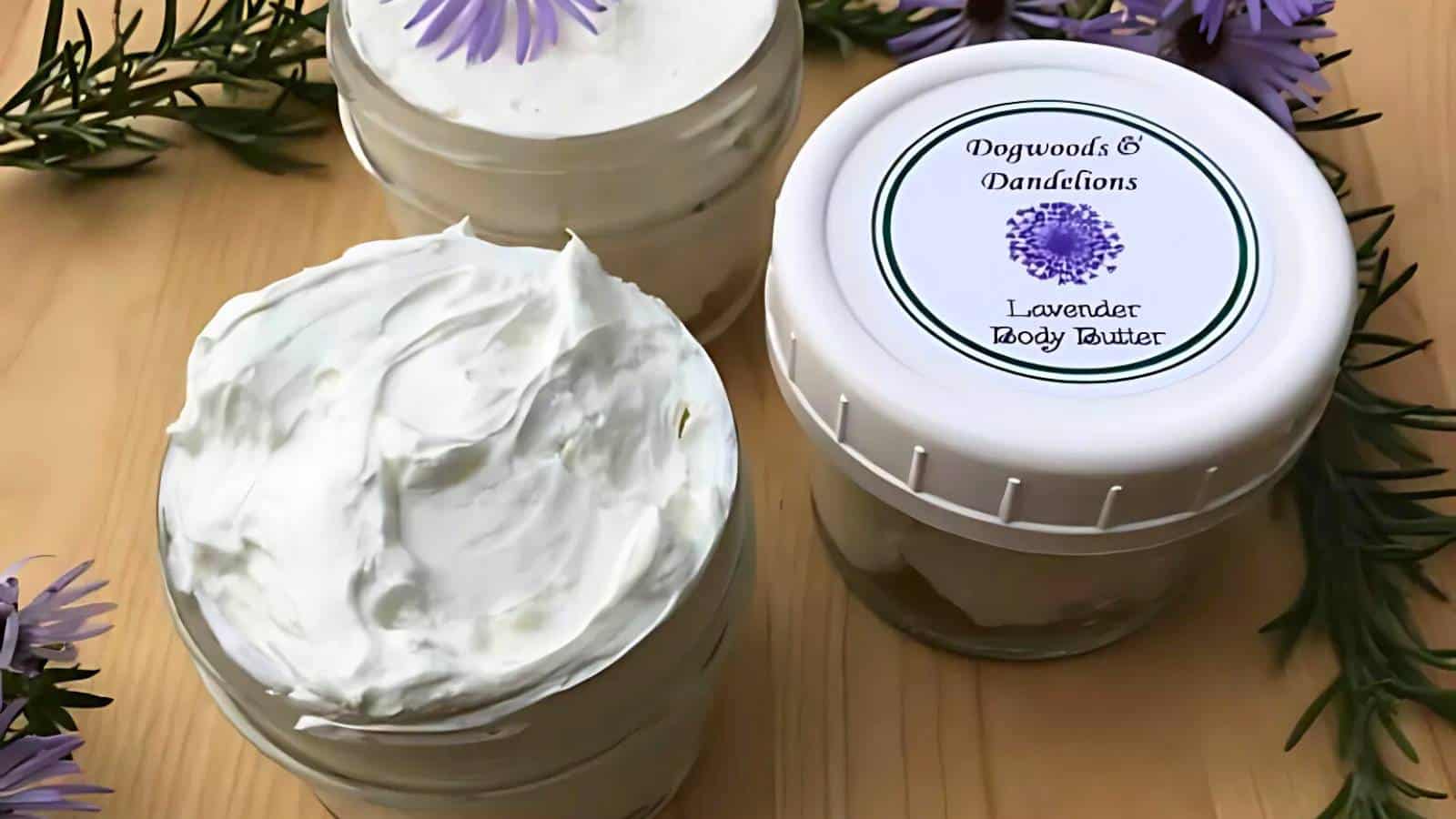 A glass jar filled with a thick white cream, placed on a wooden surface, surrounded by purple flowers and green sprigs.