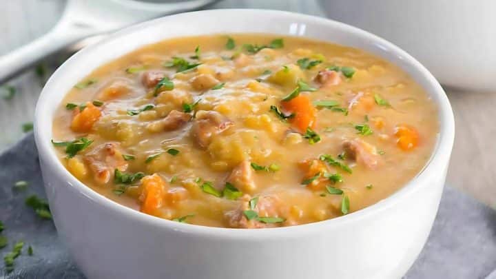 A white bowl filled with creamy split pea soup, garnished with chopped herbs.