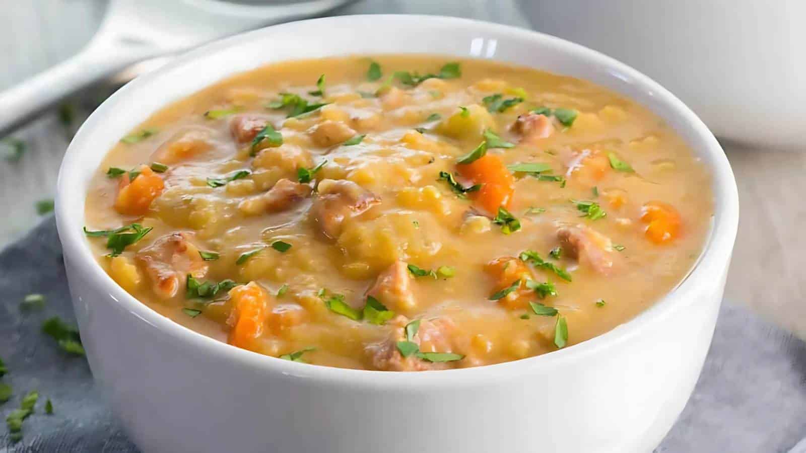 A white bowl filled with creamy split pea soup, garnished with chopped herbs.