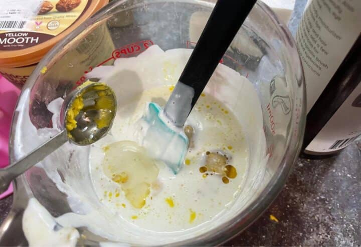 A bowl filled with DIY shampoo bar ingredients and a spoon mixing in castor oil.