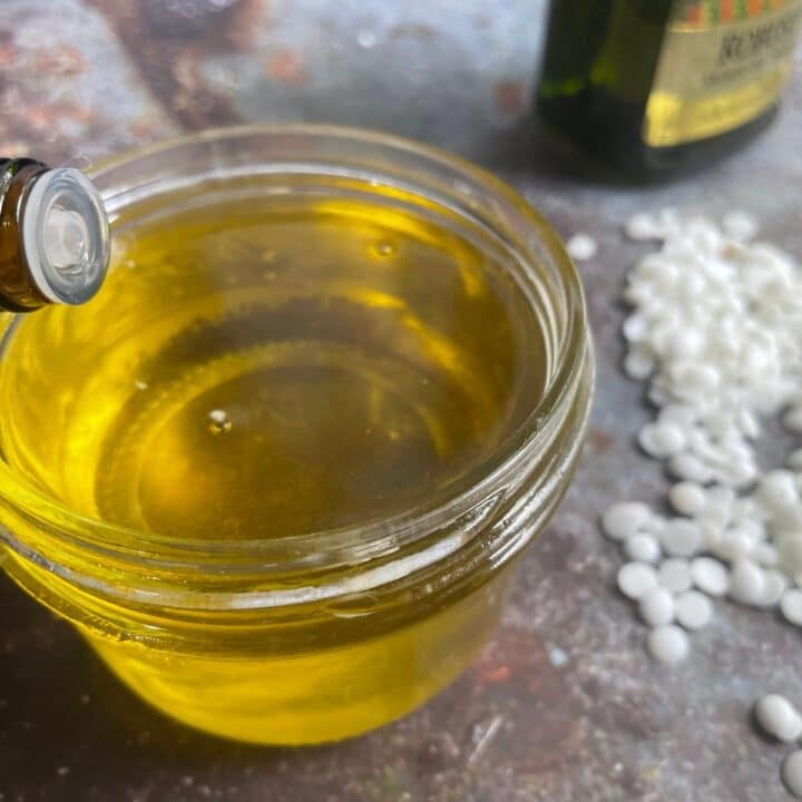 Olive oil being poured into a jar with beeswax pellets.