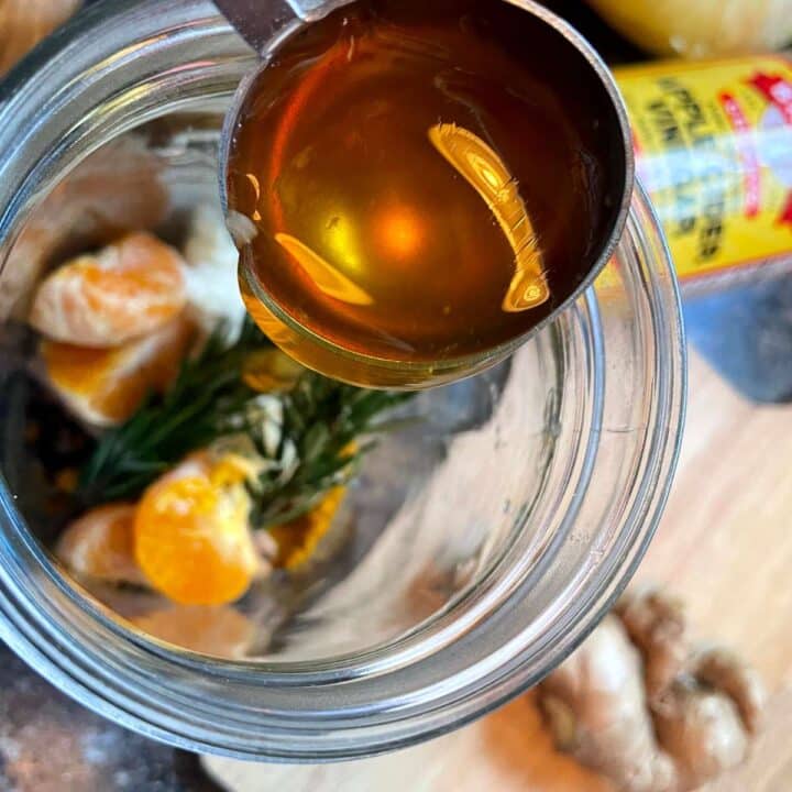 A jar of honey, ginger, and garlic with a spoon.