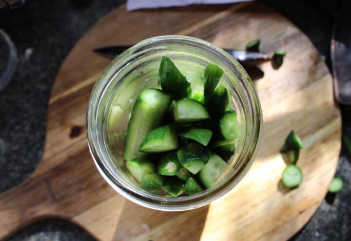 Adding sliced cucumbers to mason jar for pickles.