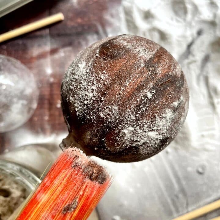 A person is holding a wooden ball with a stick in it.