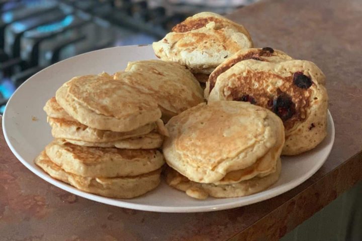 A plate of homemade almond milk pancakes, some with blueberries, sits on a kitchen countertop.