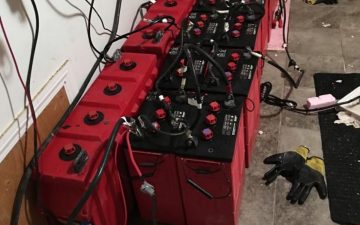 a picture of a few dozen red surrette batteries connected by cables in series.