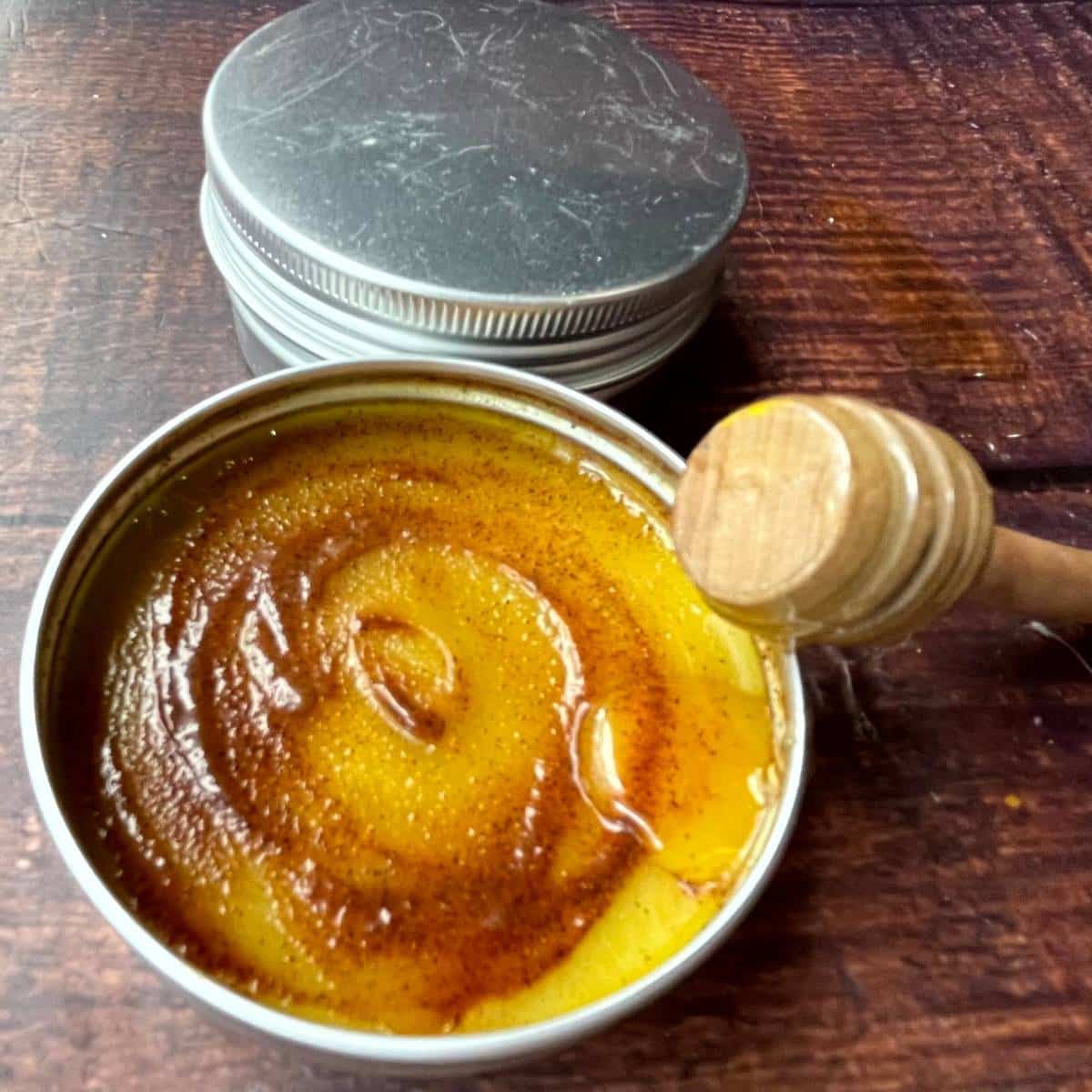 A tin of beeswax and coconut oil lip balm with a wooden spoon next to it.