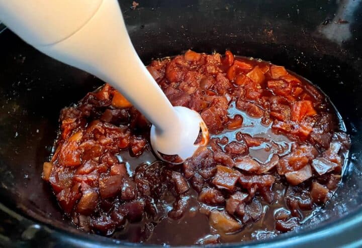 A spoon is being used to stir the meat in a slow cooker.
