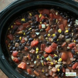 a black bean soup with tomatoes and corn in a black slow cooker