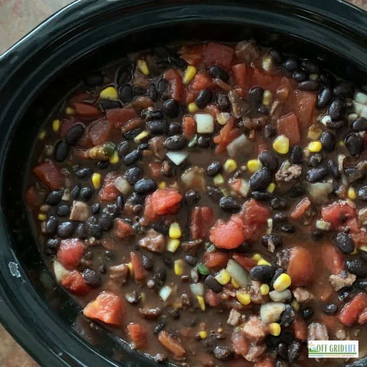 a black bean soup with tomatoes and corn in a black slow cooker