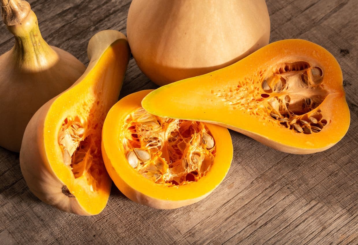 A squash is cut in half and sitting on a wooden table.