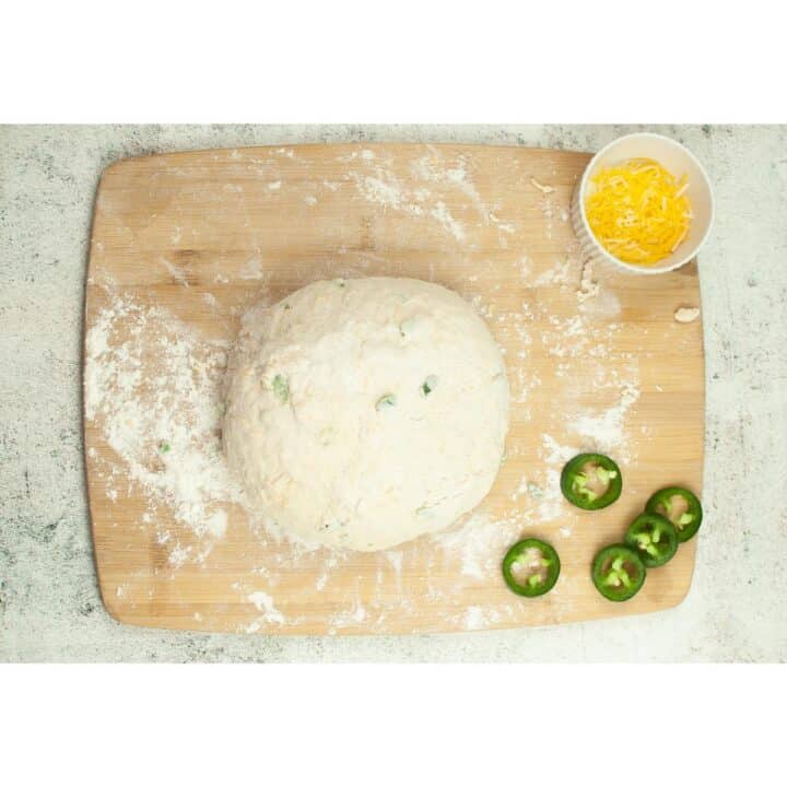 A dough on a cutting board with jalapeno peppers.