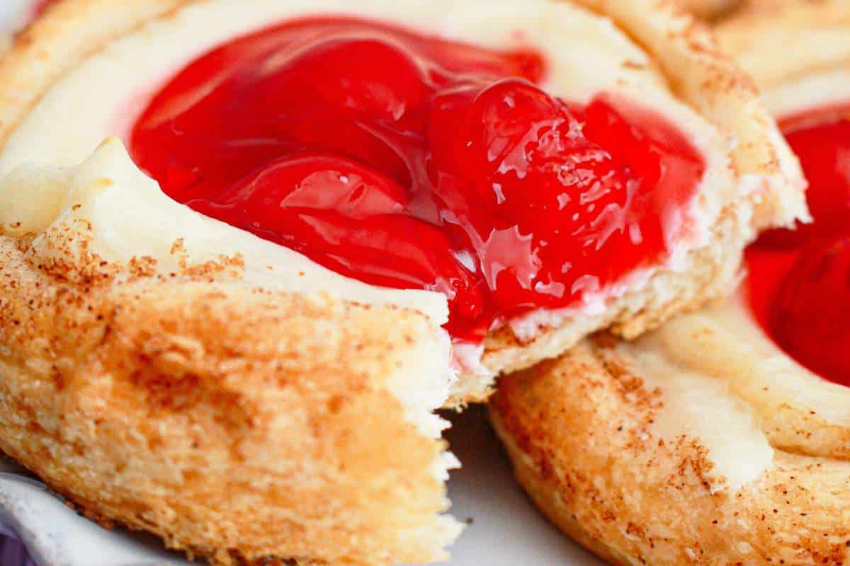 A close-up view of a pastry with a creamy filling and a dollop of red cherries on top.
