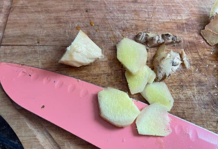 Ginger slices on a cutting board with a pink knife.