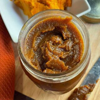 Pumpkin butter in a jar on a cutting board.