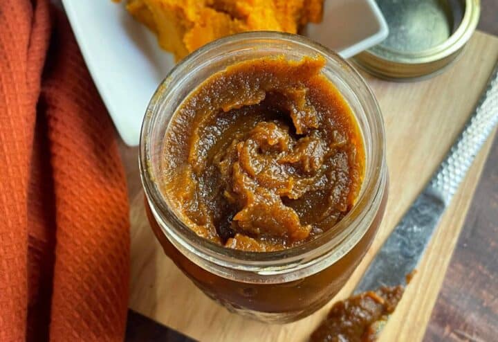 Pumpkin butter in a jar on a cutting board.