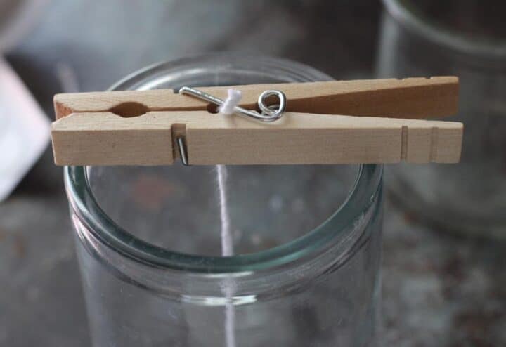 Clothes pegs and wick over a glass candle jar.