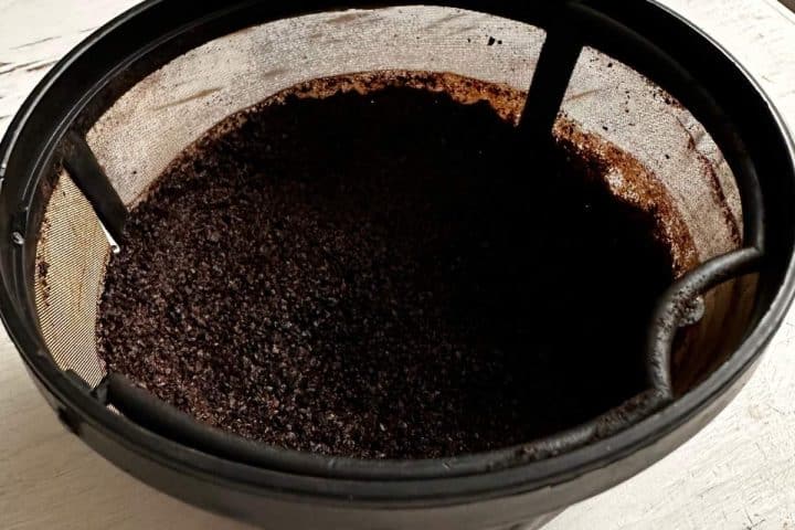 A close-up of used coffee grounds in a reusable coffee filter for DIY compost starter.