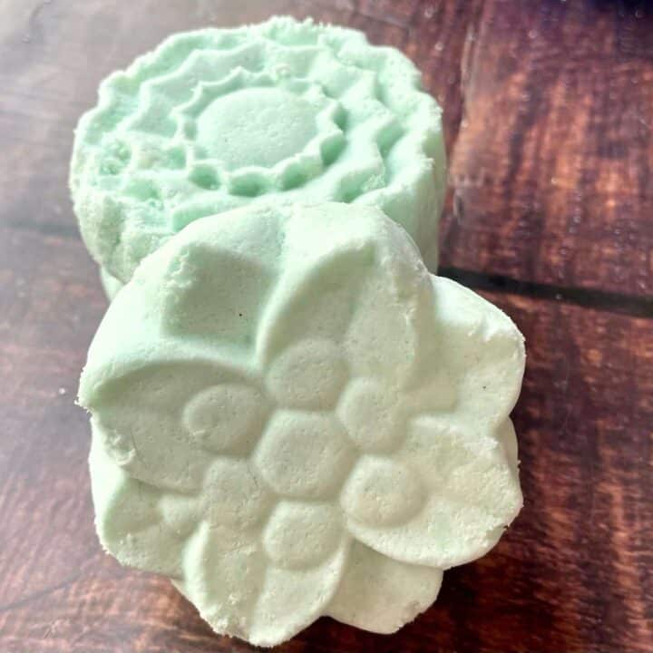 Two green soaps on top of a wooden table.