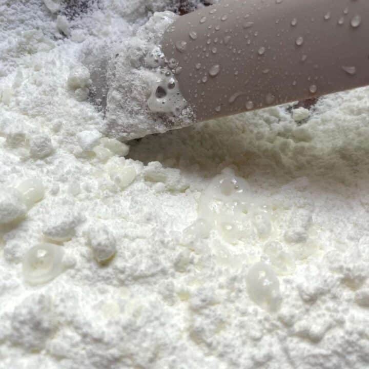 A person is sifting ingredients into a bowl.