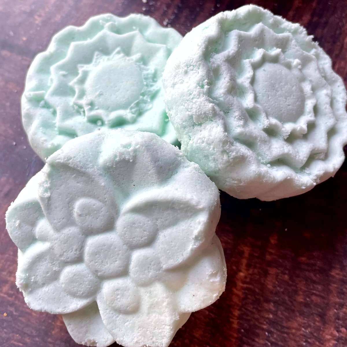 Three green aromatherapy shower steamers sitting on top of a wooden table.