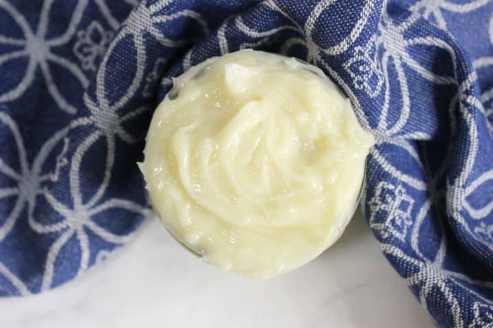 A small jar filled with cDIY hair butter, sits on a blue patterned cloth.