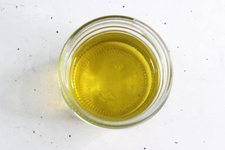 Top view of a clear glass jar containing yellow oil, placed on a white speckled surface.